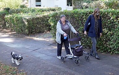 Ältere Dame mit Rollator und Hund in Begleitung einer Frau