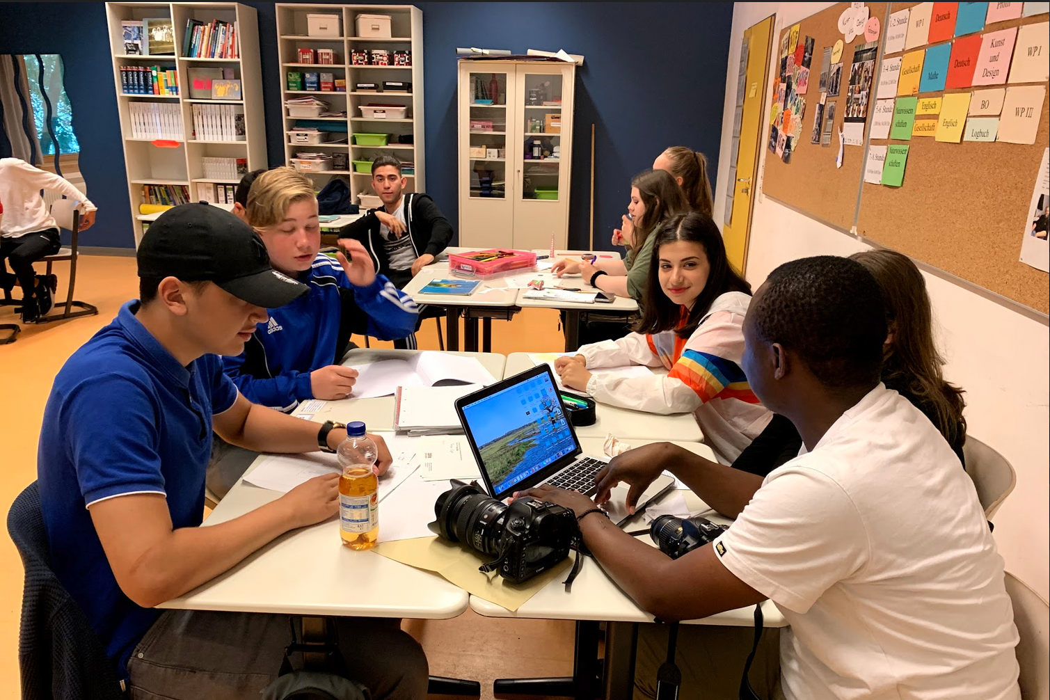 Foto: Schülerinnen und Schüler mit Laptop an zwei Tischen
